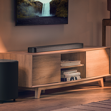 JBL Bar 500MK2 pe o comodă TV, cu subwooferul alături, sub un televizor de perete