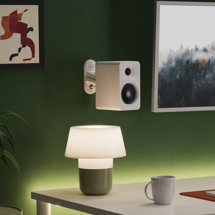 Boxă Kanto Audio ORA albă montată pe perete cu un suport, deasupra unui birou