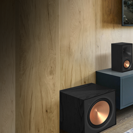Boxa de centru Klipsch R-50C langa o boxa de raft si un subwoofer, pe fundal de lambriu de stejar