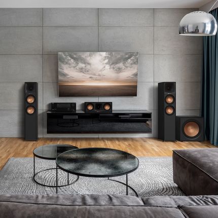 Sistem home cinema Klipsch cu boxa de centru R-50C langa un receiver AV, intre doua boxe de podea