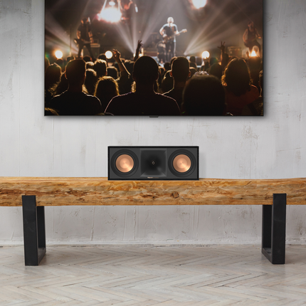 Boxa Klipsch R-50C centrata pe o banca de lemn, sub un televizor mare
