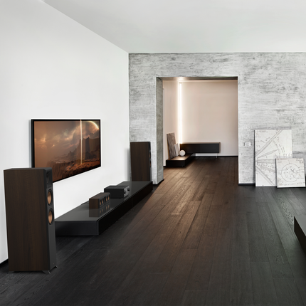 Doua boxe Klipsch RP-6000F II in Walnut incadrand un televizor, pe parchet inchis la culoare