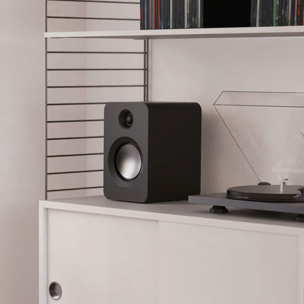 Kanto Audio REN in black on a shelf next to a turntable