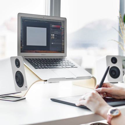 Boxe Kanto Audio YU2 albe pe un birou, lângă un laptop și un microfon