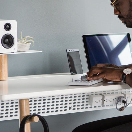 Boxă Kanto Audio YU2 albă pe un raft de birou din lemn, lângă un computer
